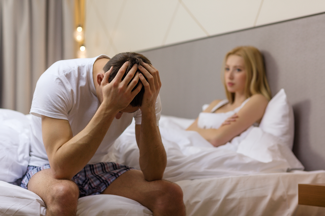 Homem preocupado e mulher o olhando sentados na cama | O que causa a ejaculação precoce?