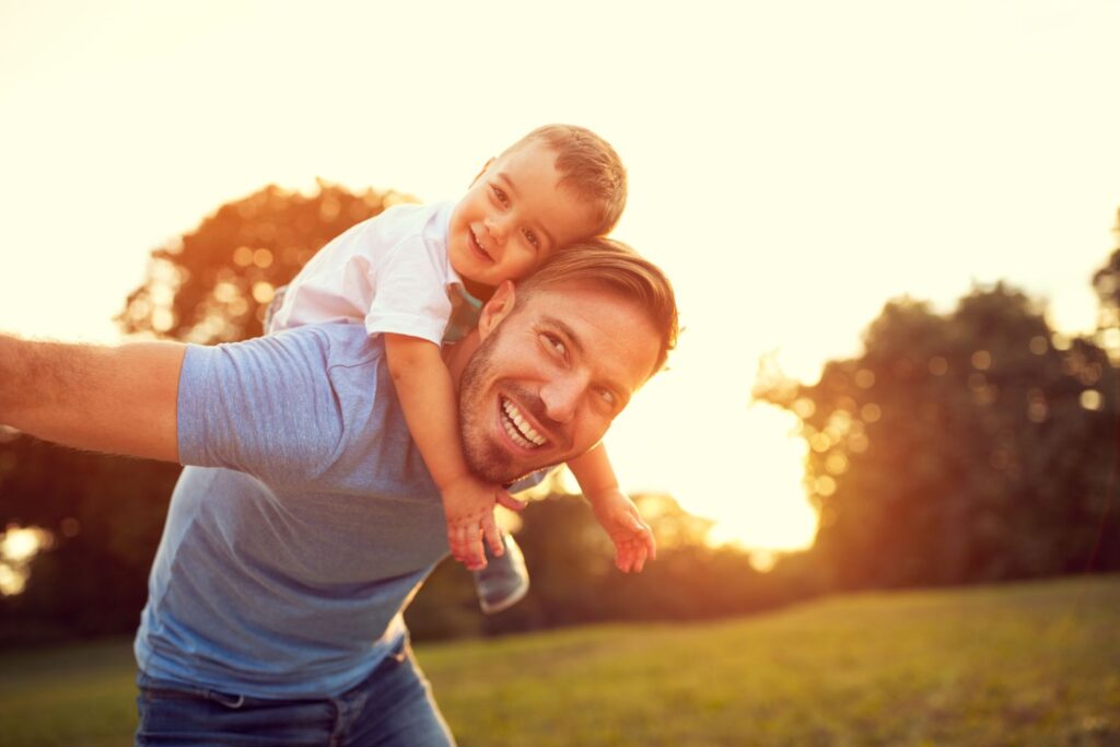 Homem sorrindo com o filho nas costas | Câncer de Próstata: é possível reduzir as minhas chances de ter?